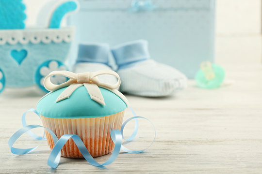 Tasty cupcakes with bow and baby shoes, decorative baby carriage and photo album  on color background