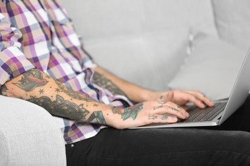 Obraz premium Young man with tattoo using laptop on a sofa at home