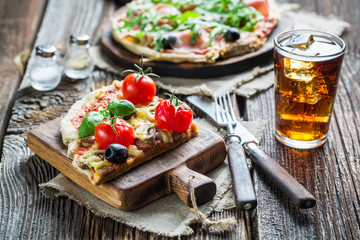 Thin pizza made of ham, olives, arugula and cold drink