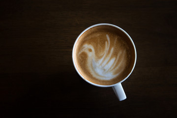 Cup of latte art coffee with froth shape bird and wooden backgro