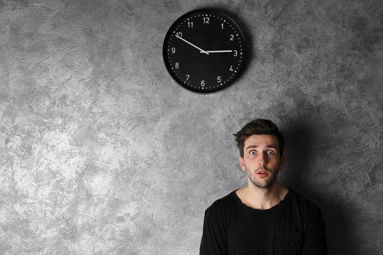 Man In A Black Shirt Standing Beside A  Big Clock On Grey Wall