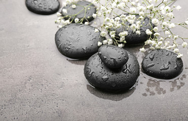 Beautiful spa composition with wet stones and flowers on grey background