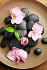 Spa stones and orchid flowers in round plate, top view
