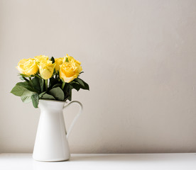 Yellow roses in white jug on white table against neutral background