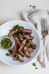 Sliced Steak served in white bowl with chimichurri sauce. Top view.