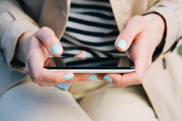 Woman in a beige dress holding a mobile phone with two hands clo