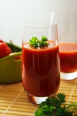 Glass of tomato juice with parsley on straw mat, close up.