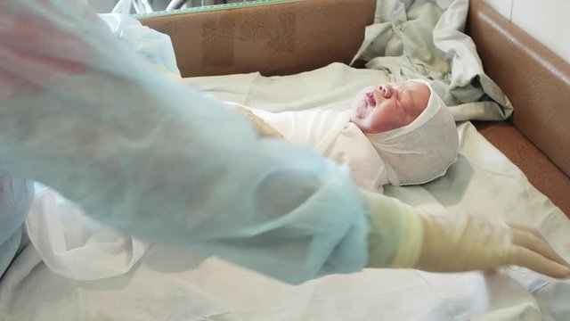 Nurse in sterile gloves swaddle newborn baby after birth on table. Diapers, blanket. Maternity hospital.