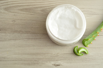White beauty cream in a jar displayed with aloe Vera on a wooden background