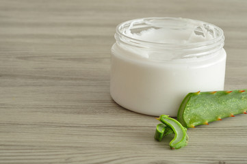 White beauty cream in a jar displayed with aloe Vera on a wooden background