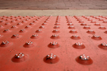 Red steel sidewalk plate with round pattern, leading to cement and bricks
