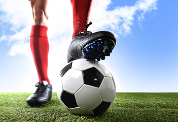 close up legs feet football player in red shocks and black shoes posing with ball standing on grass outdoors