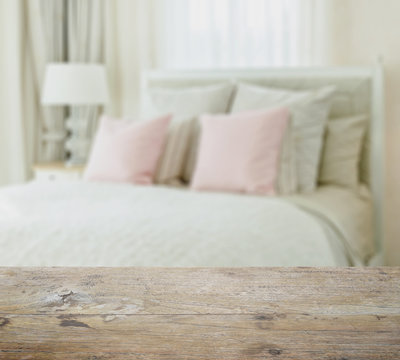 wooden table top with blur of luxury bedroom interior with pink pillows on bed