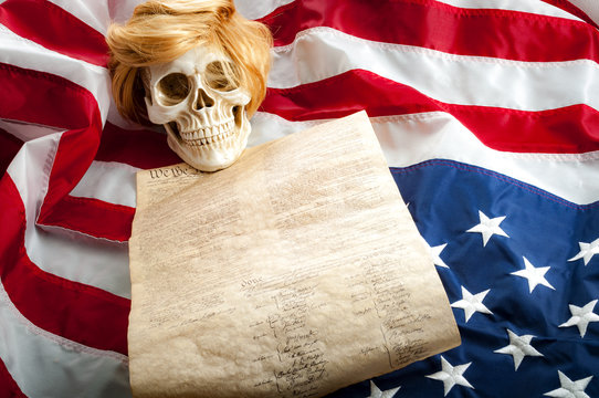 A human skull wearing a ginger wig on top of the US constitution and the upside down american flag symbolizing the danger that demagoguery, racism, manipulation and hatred can bring to freedom