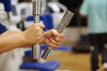 asian woman hand hold dumbbell tightly with fitness studio room background - soft focus and select focus