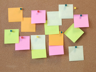 Many blank-colored sticky notes post advertise on wooden cork boards as a reminder and to write messages, communicate, plan or organize business work lists in office. All labels are still empty.