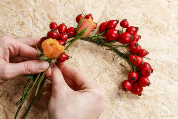 Florist at work: woman making wreath with rose hip fruits (rosa