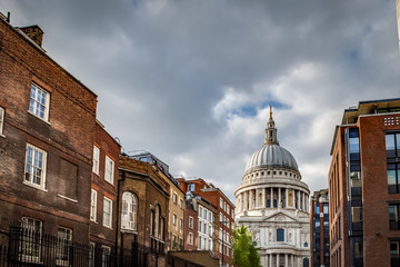 St Paul’s cathedral seen from a narrow alley enclosed by brick buildings on a cloudy day in summer