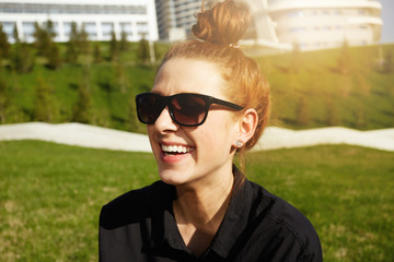 Outdoor lifestyle portrait of stylish student girl, wearing hipster sunglasses and black shirt, laughing and having fun during nice evening walk with groupmates after classes at the university.