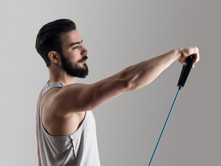 Side view of young athlete in tank top workout with elastic resistance band doing shoulder exercises.