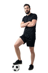 Football player standing on the ball with one leg posing with crossed arms. Full body length portrait over white background.