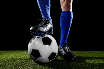 legs and feet of football player in blue socks and black shoes posing with the ball playing on green grass
