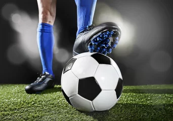 Foto auf Acrylglas legs and feet of football player in blue socks and black shoes posing with the ball playing on green grass © Wordley Calvo Stock