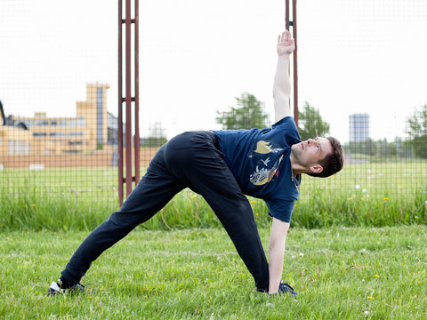 Outdoor yoga workout. Young man doing an exercise in the city park, turning triangle pose