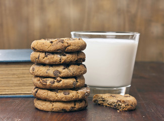 Stack of chocolate chips cookies with milk and old book