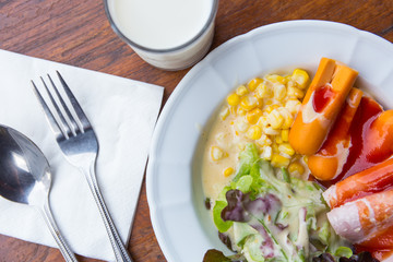 Morning vegetable salad with hotdog on dish and milk on wooden t