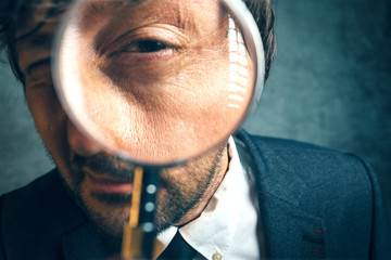 Enlarged eye of tax inspector looking through magnifying glass. Businessman with loupe inspecting documents.