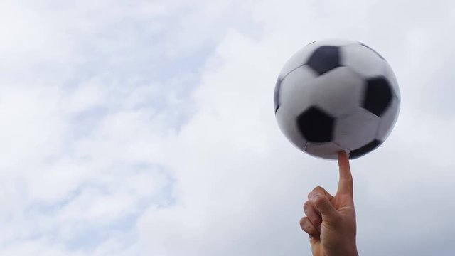 4K Football or soccer ball spinning on a finger against a sky background, in slow motion, with space for text