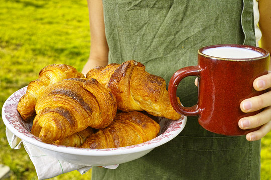 Young woman holding mug witn organic milk and fresh baked croiss