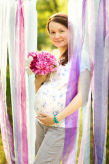 Beautiful pregnant woman with a bouquet of flowers relaxing outside in the park
