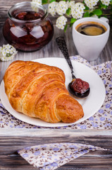 Closeup freshly baked  croissant with strawberry jam and coffee cup  on vintage rustic tray. Breakfast concept.