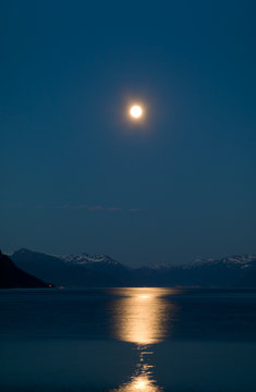 Full moon above snow-clad mountains reflected in a Norwegian fjord