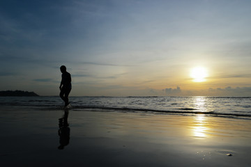 Silhouette of a Boy Walking on the beach at sunset backdrop.