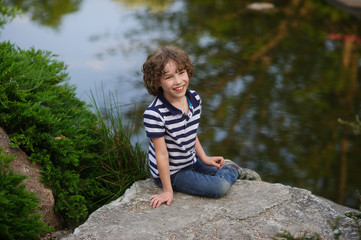 Naklejka na ściany i meble Cute little boy sitting on the shore of a small lake