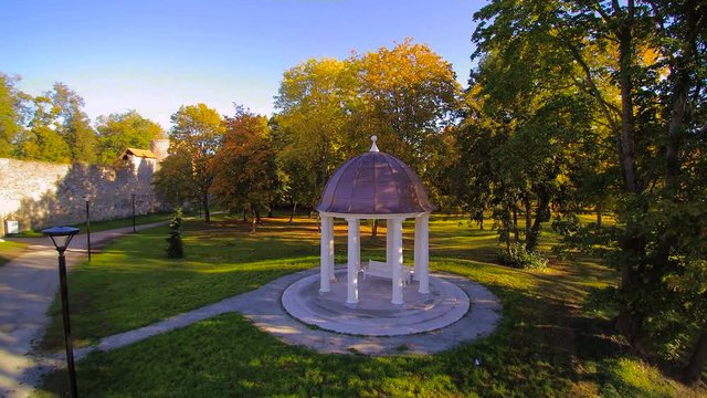 The bower or gazeebo in the grassy yard with trees surrounding the park and a bench inside the bower