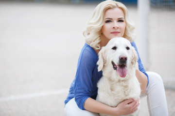 Beautiful woman with curly blonde hair and brown eyes wearing a blue shirt and white jeans,spends time on the football field in the summer,playing with your favorite dog breed Golden Retriever