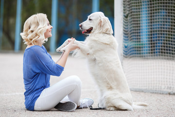 Beautiful woman with curly blonde hair and brown eyes wearing a blue shirt and white jeans,spends time on the football field in the summer,playing with your favorite dog breed Golden Retriever