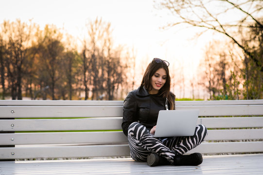 Close portrait of gorgeous dark-hair woman student using laptop computer at campus, charming female teenager studying on park bench with open net-book, exam preparation