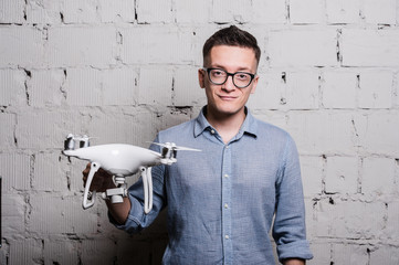 Young stylish Man in glasses with quadcopter drone on a grey brick wall