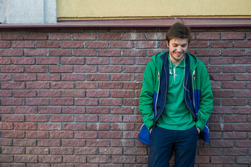 Fototapeta na wymiar Common young man wearing green t-shirt jacket and jeans against a red brick wall looking to the camera