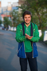 Young man walking around city listening to music with ear headphones looks at the camera and smiling. Close-up shot. Sunset. Autumn weather.