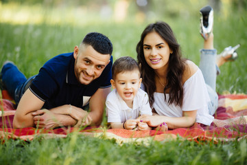 Mother, father and son lying on the grass in park on picnic. Summer family holiday