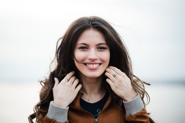 Fototapeta premium Close-up portrait of young happy beautiful attractive woman wearing leather coat smiling and standing over light outdoors background.