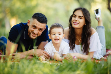 Mother, father and son lying on the grass in park on picnic. Summer family holiday