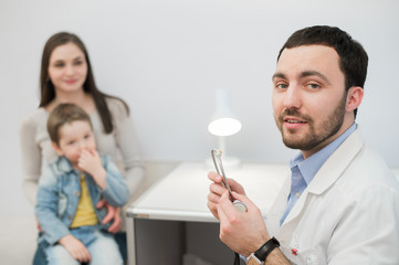 Portrait of family Doctor with stethoscope at his office. Mother and her son on the background 