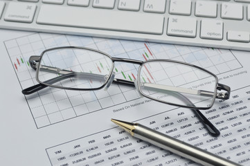 Glasses, pencil and keyboard on stock market graph, financial co
